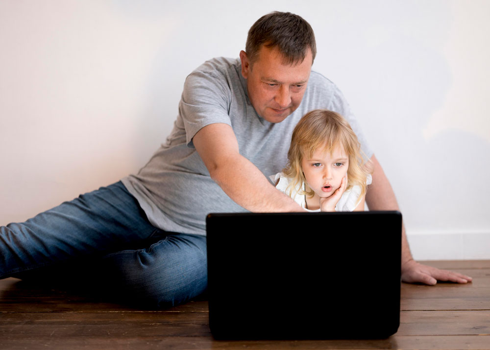 Vater und Tochter sitzen gemeinsam vor dem Laptop.