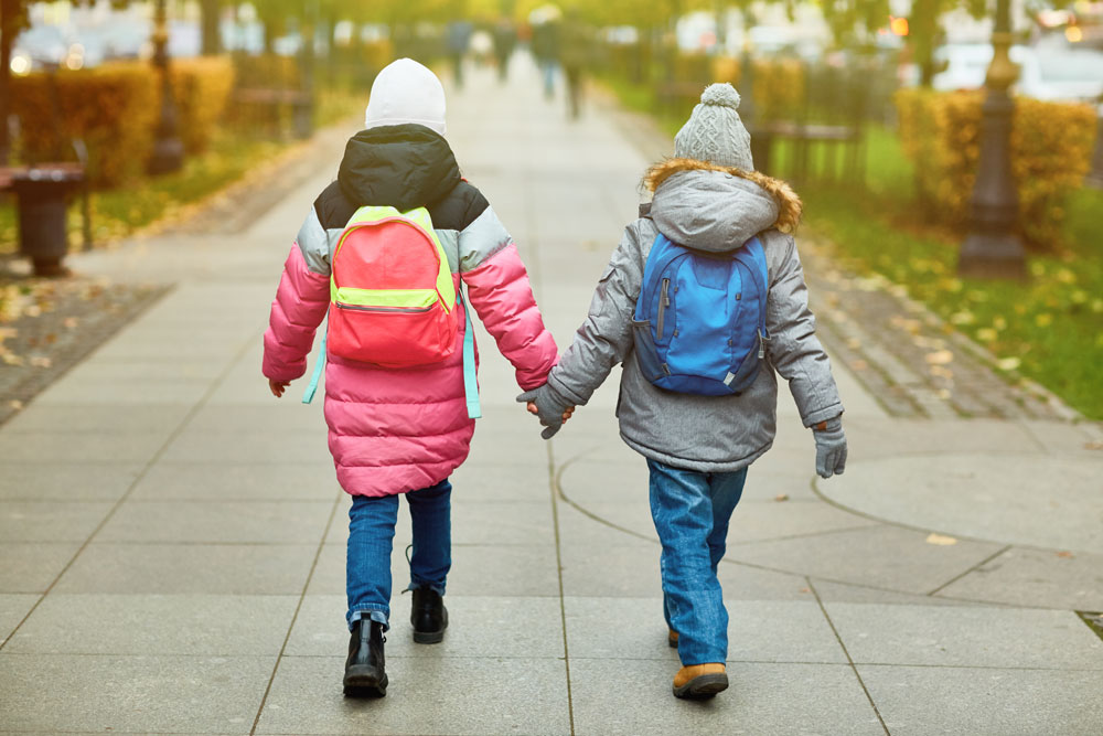 Zwei Kinder gehen Hand in Hand zur Schule