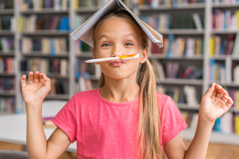 Fröhliches Mädchen mit Buch auf dem Kopf und Stift über der Lippe