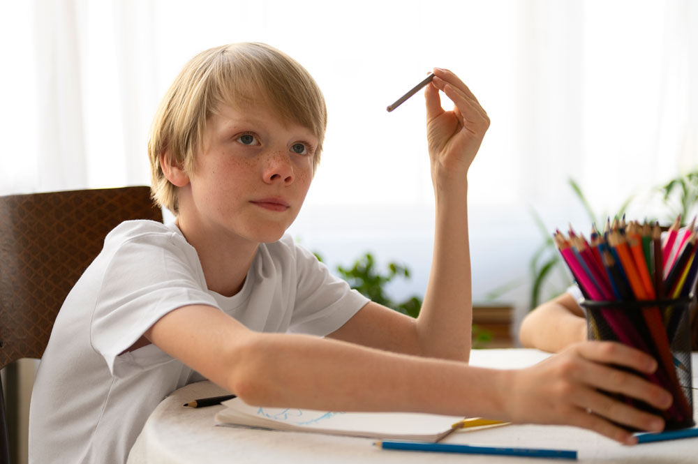 Junge sitzt am Tisch und sortiert selbstständig bunte Stifte