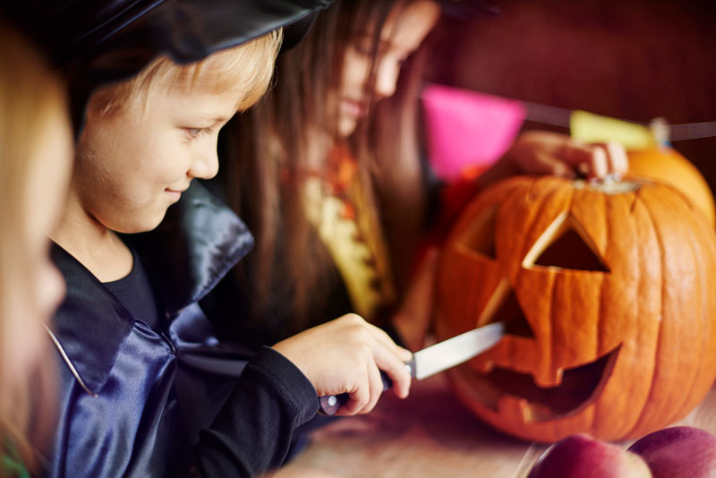 Kind im Kostüm schnitzt einen Kürbis