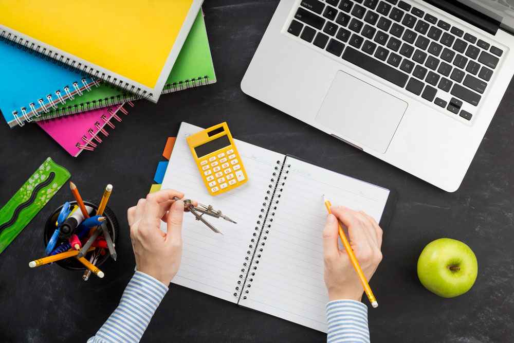Mathe lernen am Schreibtisch mit Taschenrechner, Heft und Laptop – Vorbereitung auf Mathematikübungen.